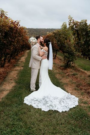 A couple shares a romantic moment in a vineyard during autumn, with the bride wearing a flowing lace train wedding dress.