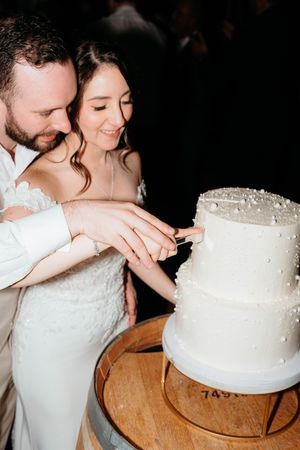 A couple cuts into their elegant white tiered wedding cake together during their reception celebration.
