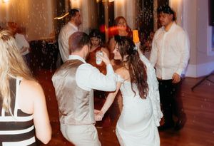 Couples dance together on a wooden dance floor at an indoor reception venue with warm lighting.