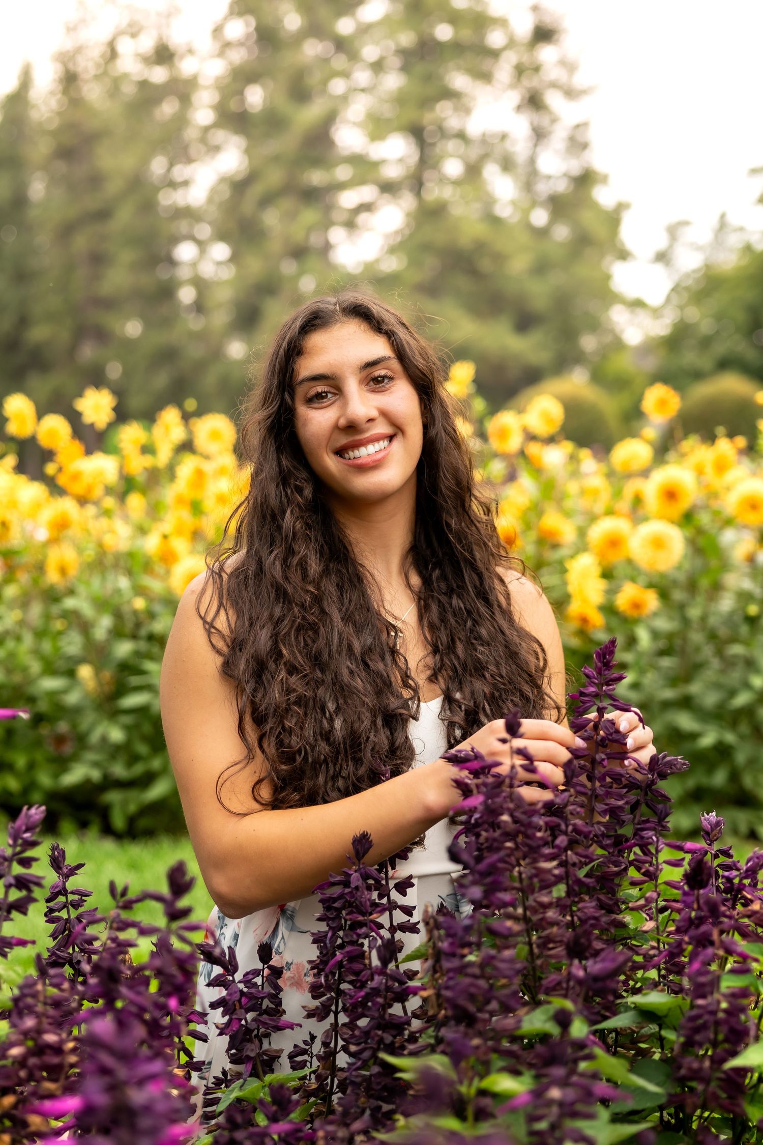 A joyful portrait in a garden with vibrant yellow sunflowers and purple salvia flowers in the background.