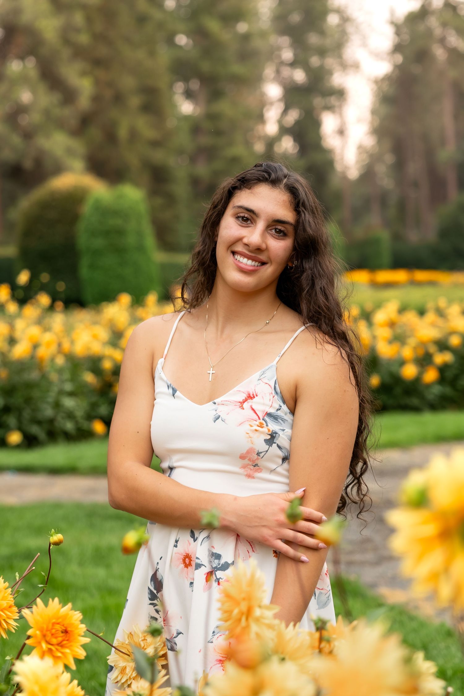 A person in a white floral dress poses among vibrant yellow daylilies in a summer garden setting.