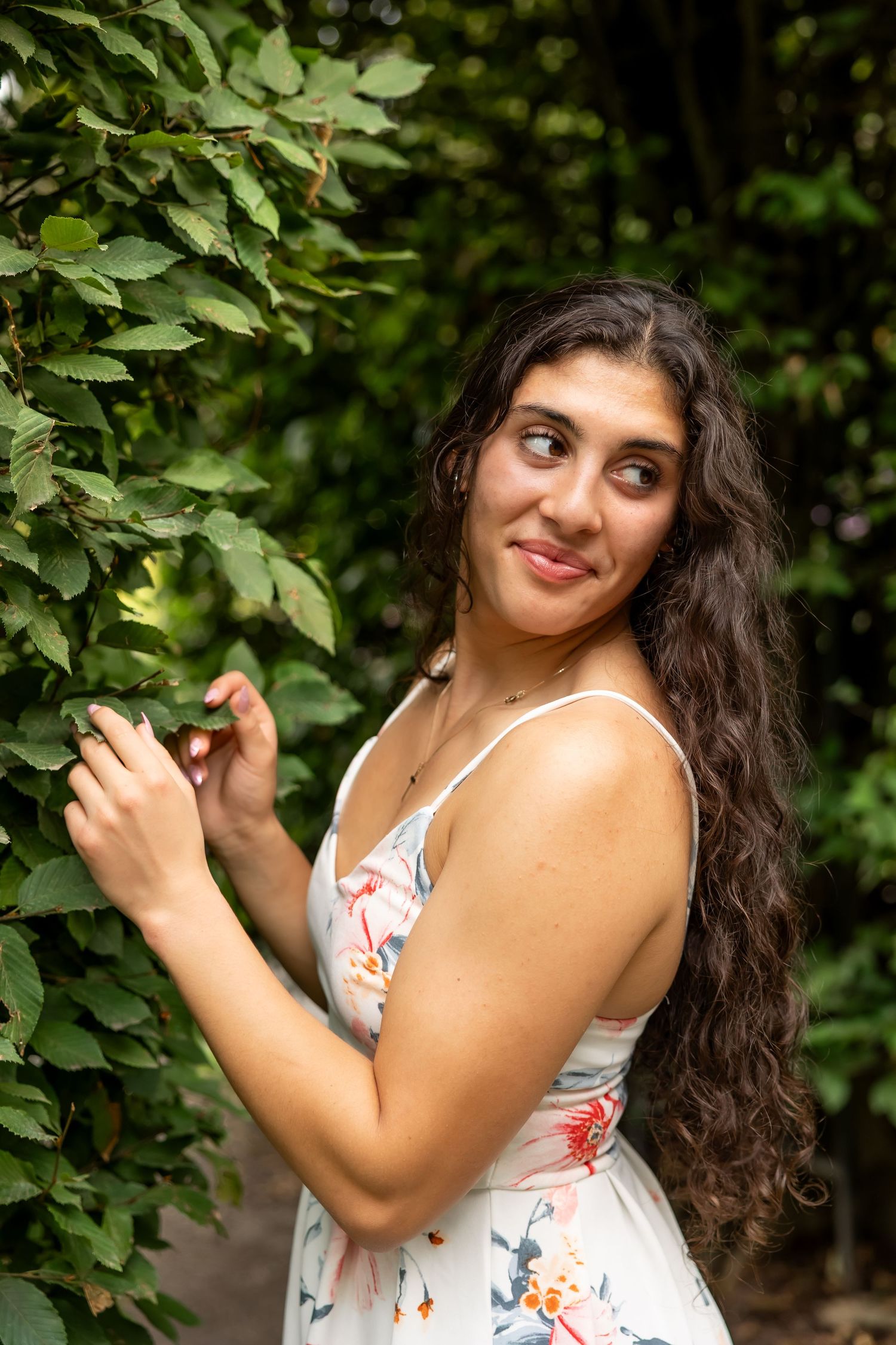 A person in a floral summer dress poses against green foliage in an outdoor photoshoot.