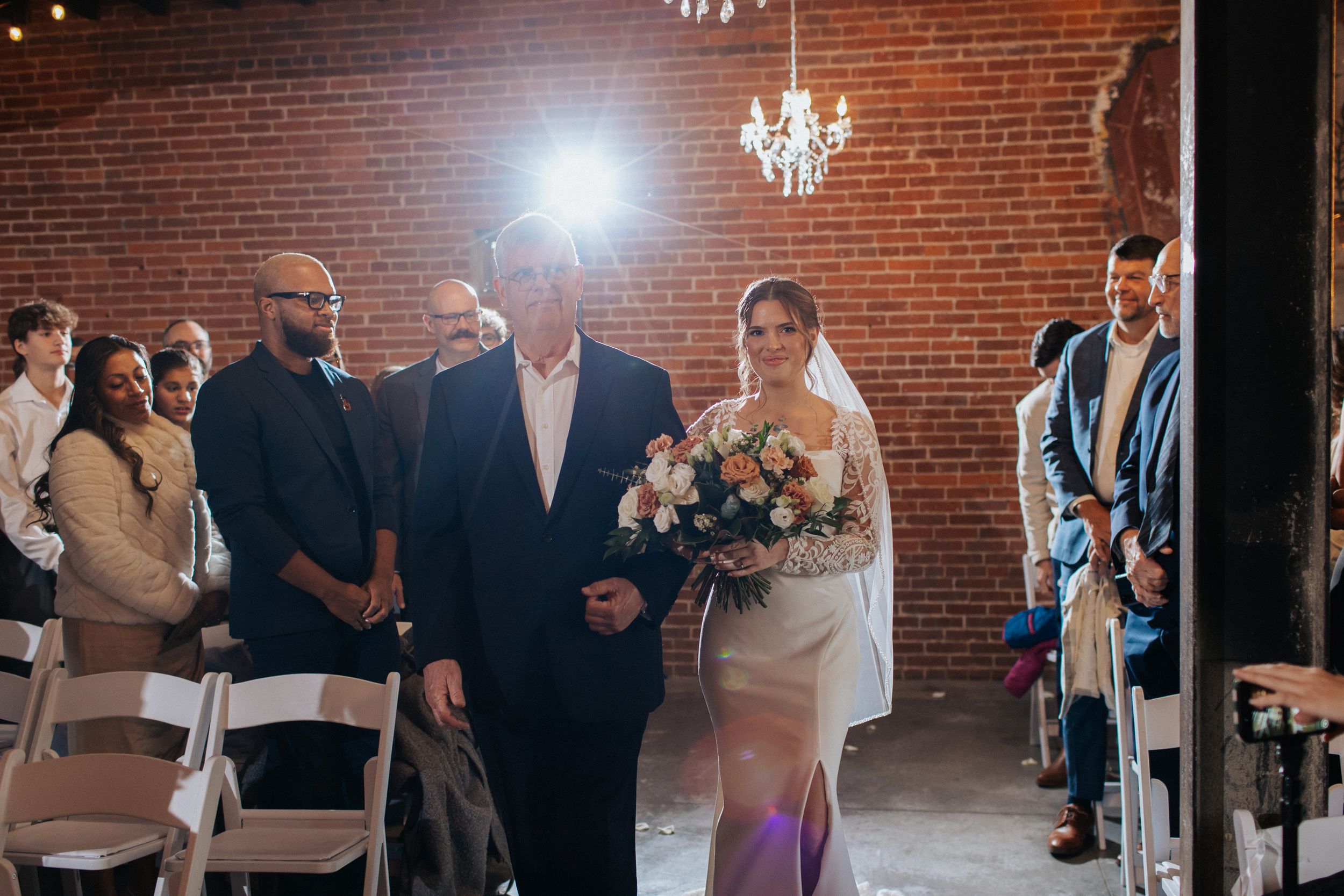 Wedding ceremony in a rustic brick venue with chandeliers and natural lighting.