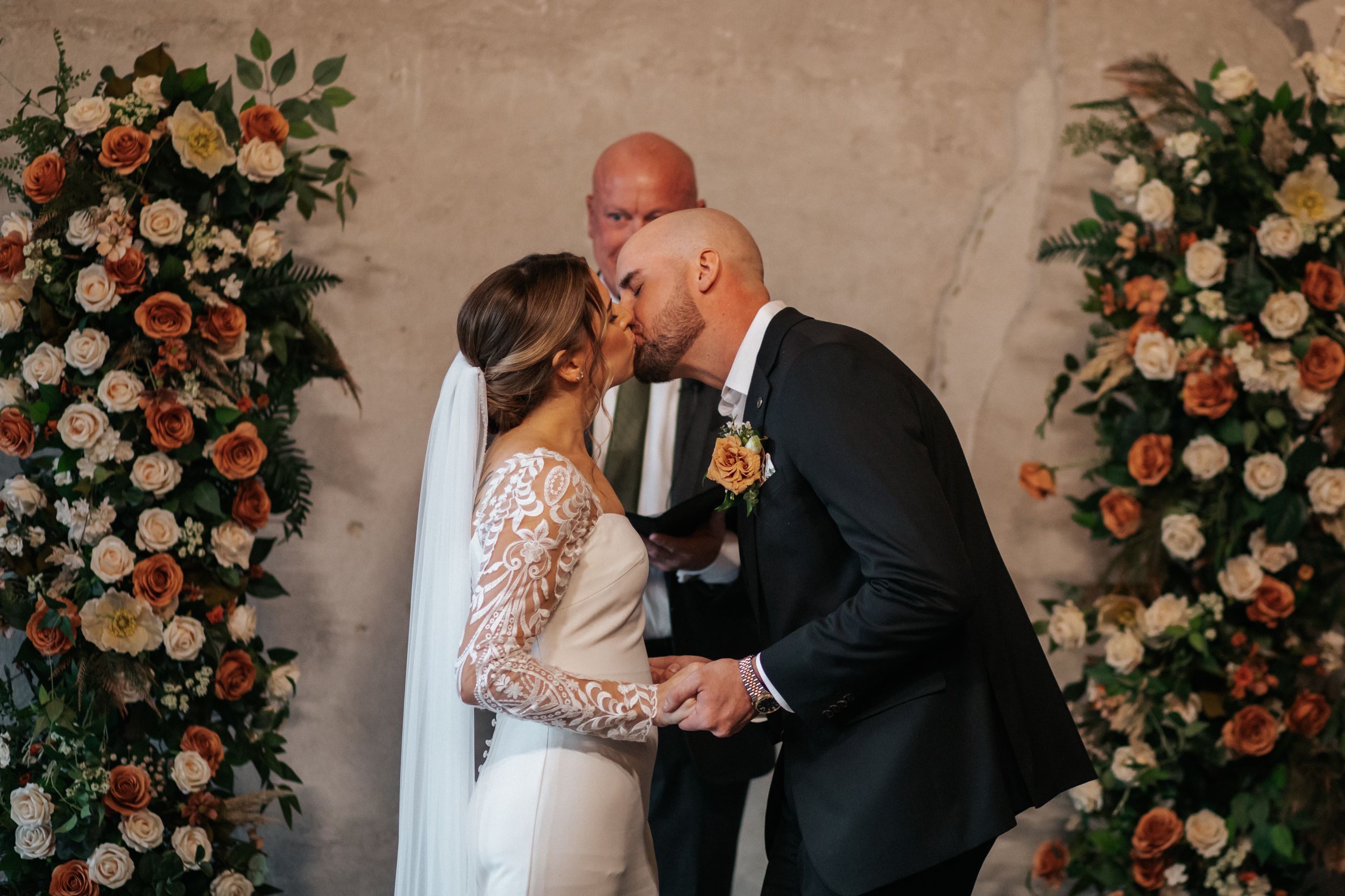 A romantic wedding ceremony moment with floral arrangements of peach roses and white flowers framing the scene.