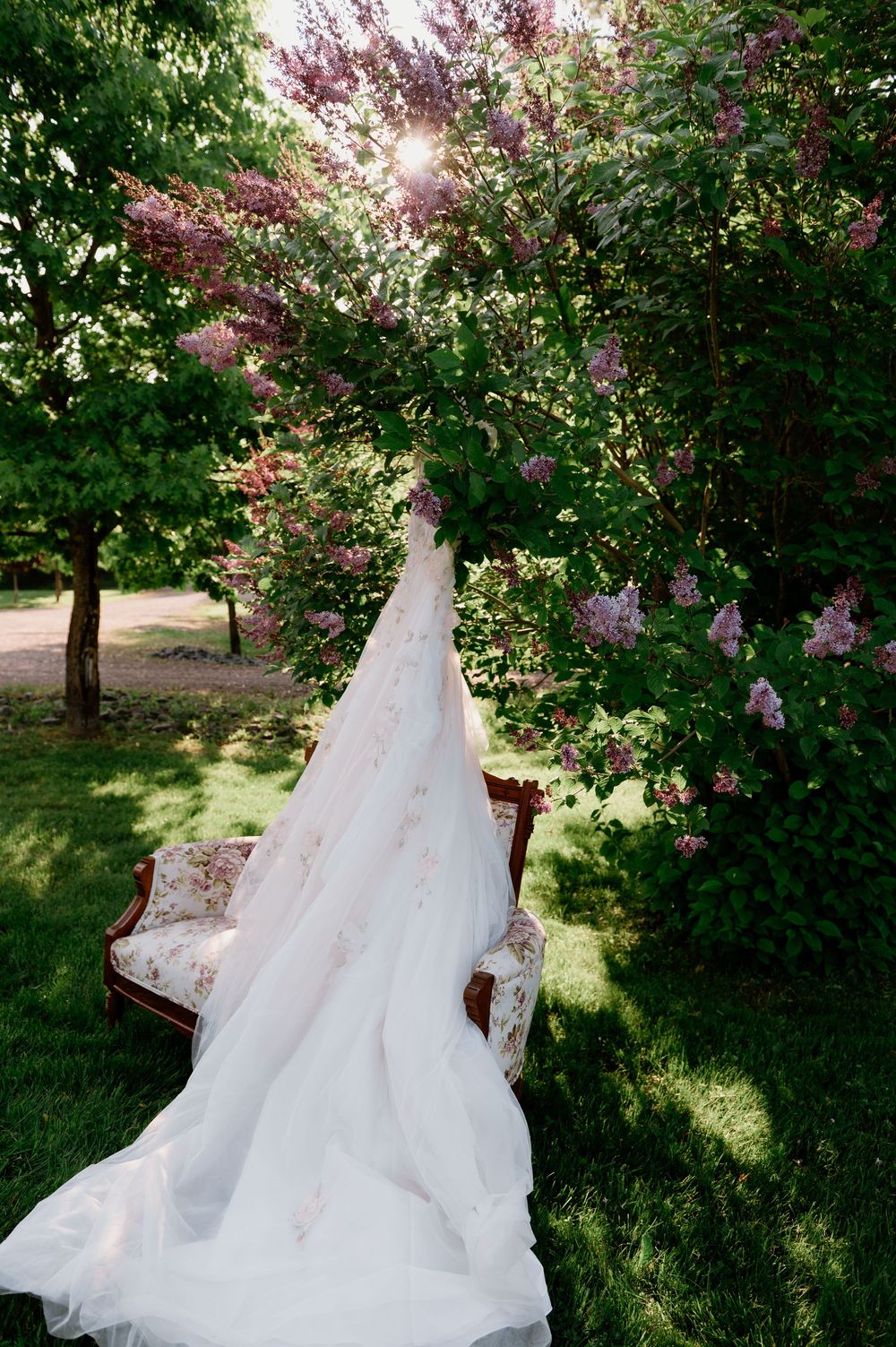 An elegant white wedding dress displayed outdoors against blooming spring lilac trees.