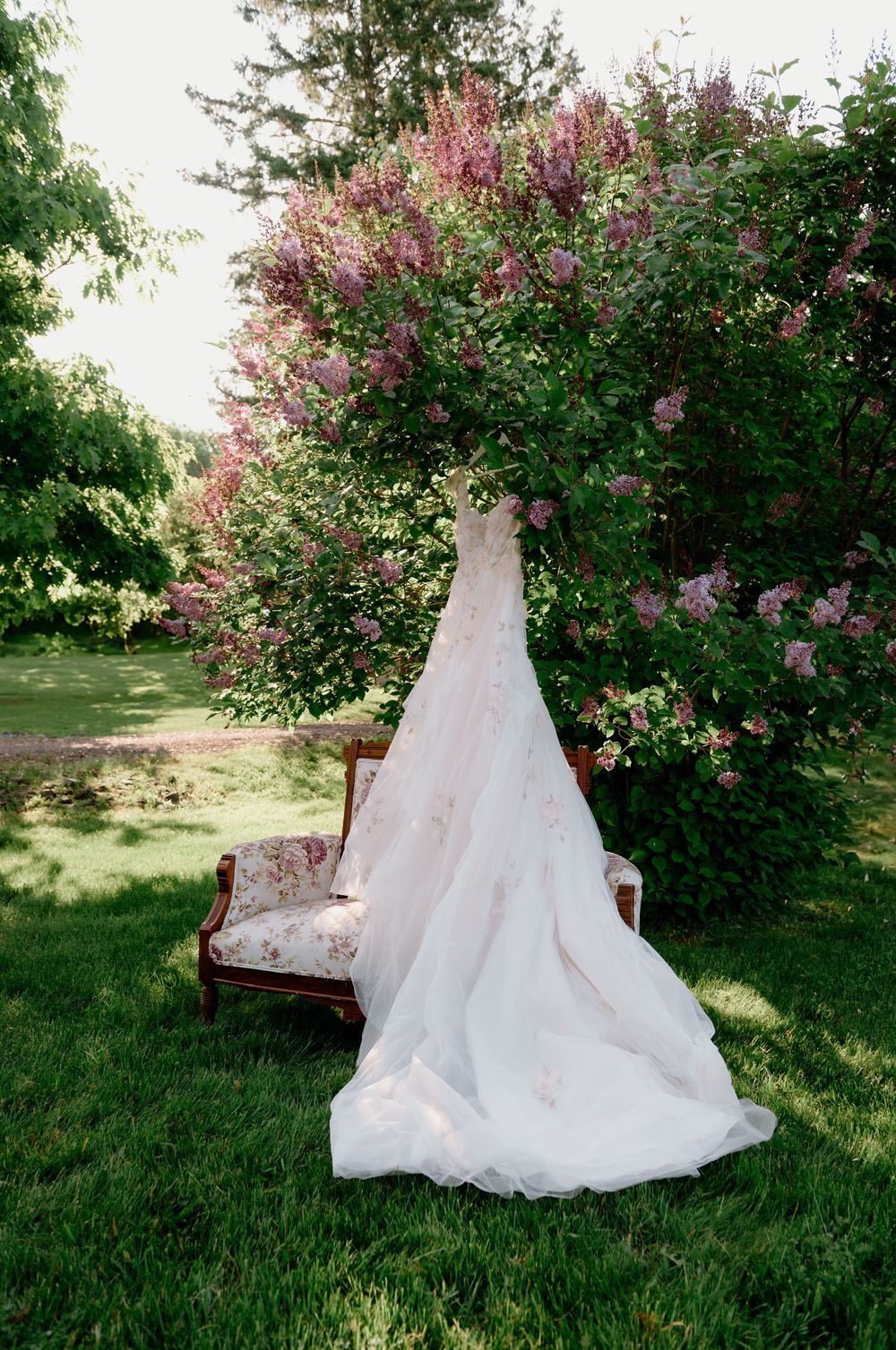 A wedding gown elegantly arranged in a garden setting with flowering lilac bushes.