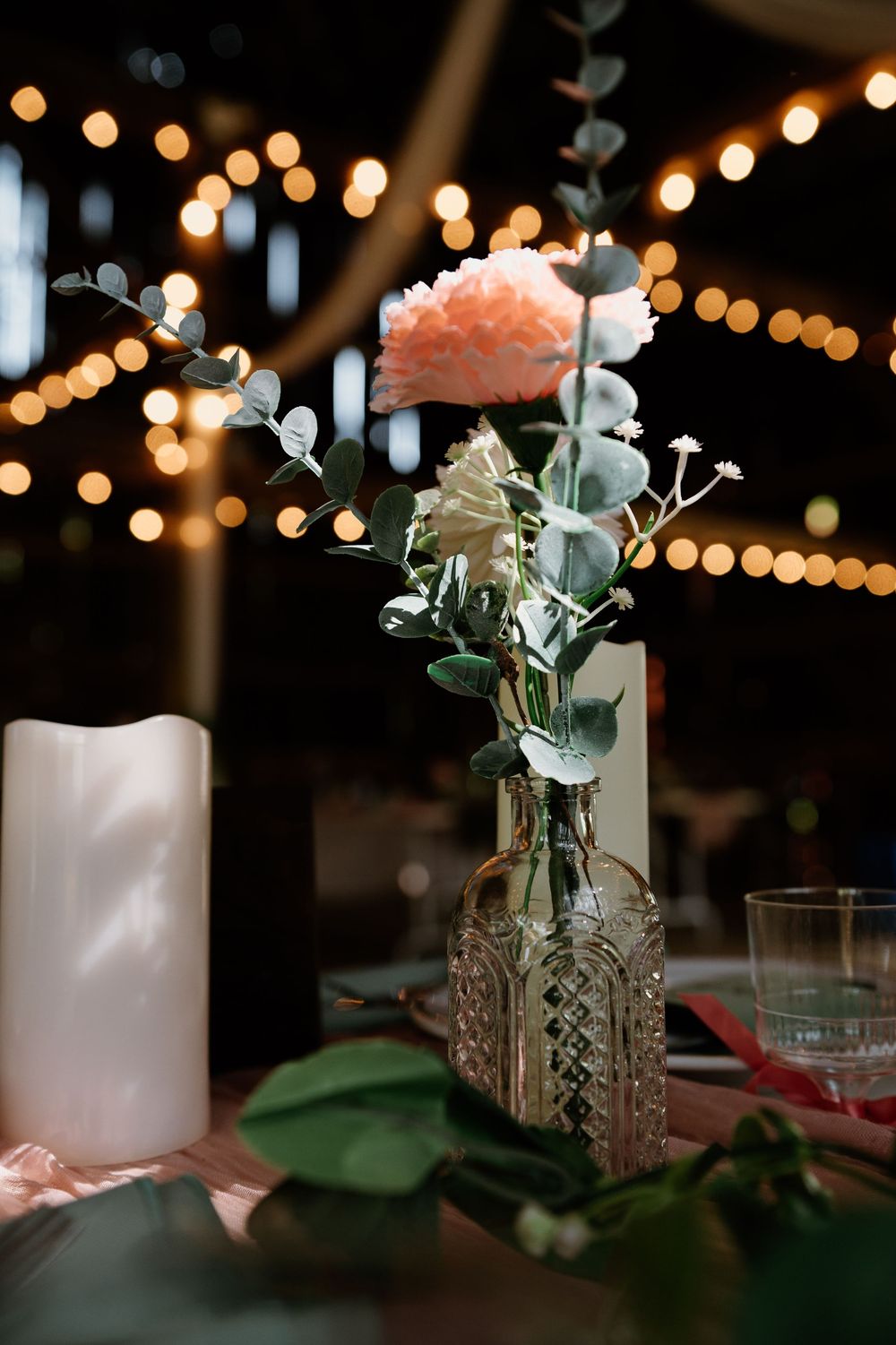 Elegant wedding table centerpiece with delicate flowers and string lights overhead.