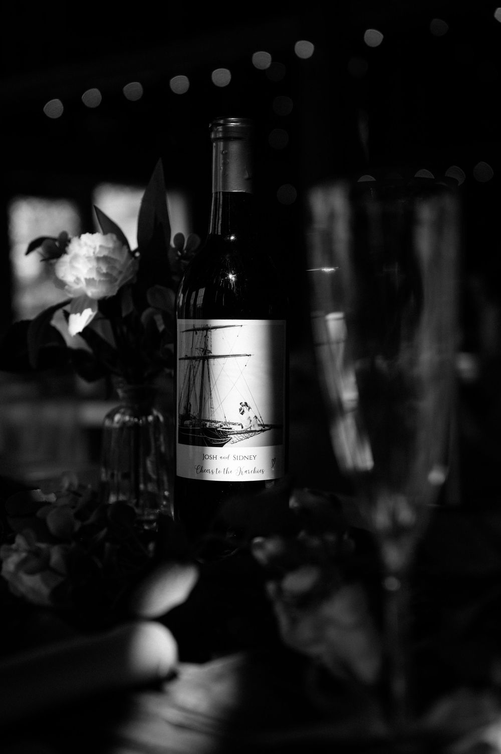 Moody black and white photograph of wine bottles lined up at an event.