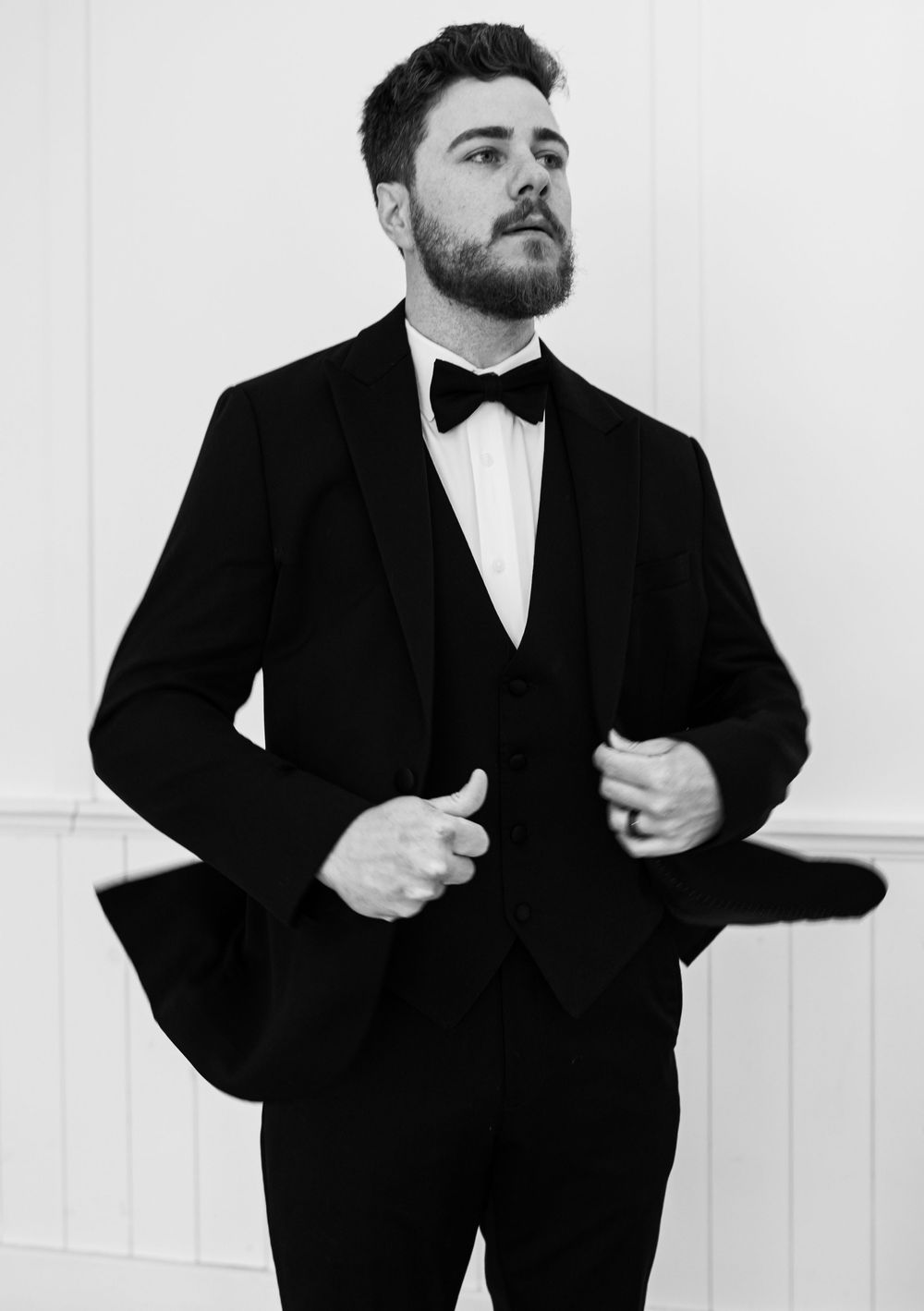 A groom in formal black attire poses against a white studio backdrop.