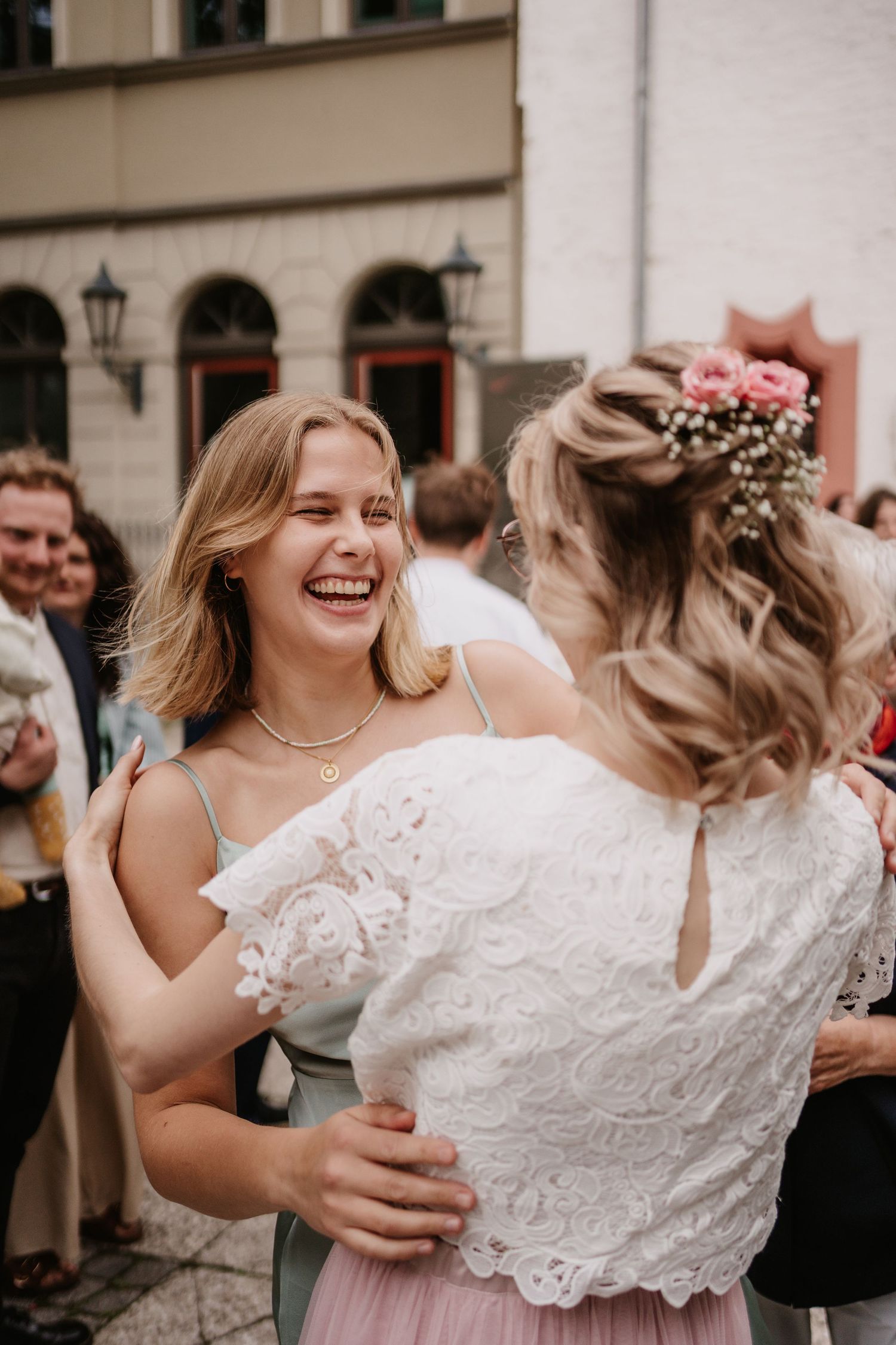 A joyful wedding party shares laughter and embraces in a candid moment during outdoor celebrations.