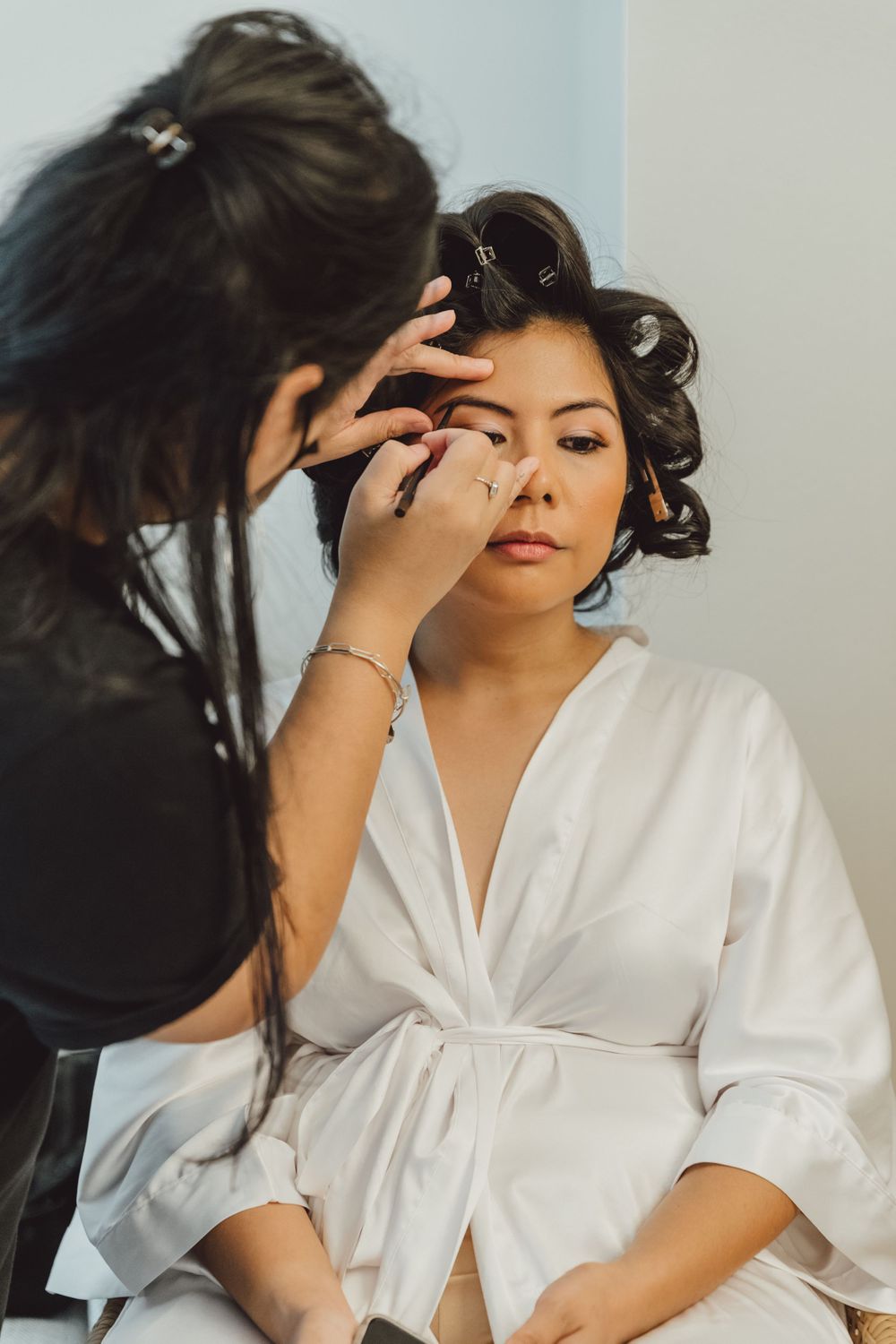 Behind-the-scenes bridal makeup preparation in white silk robe.