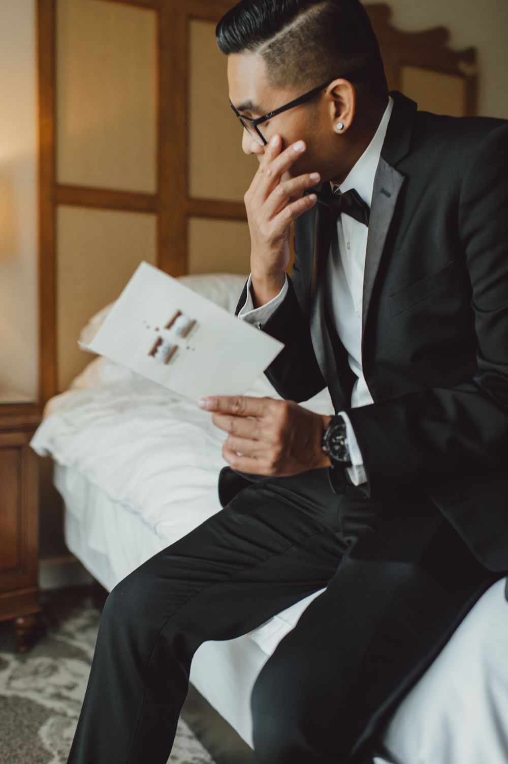 Emotional wedding moment as groom reads letter in formal black suit and glasses.