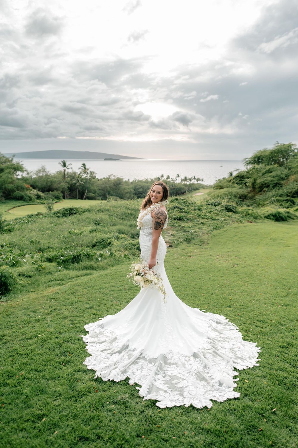 Stunning bridal gown with intricate lace train spreads across green hillside landscape.