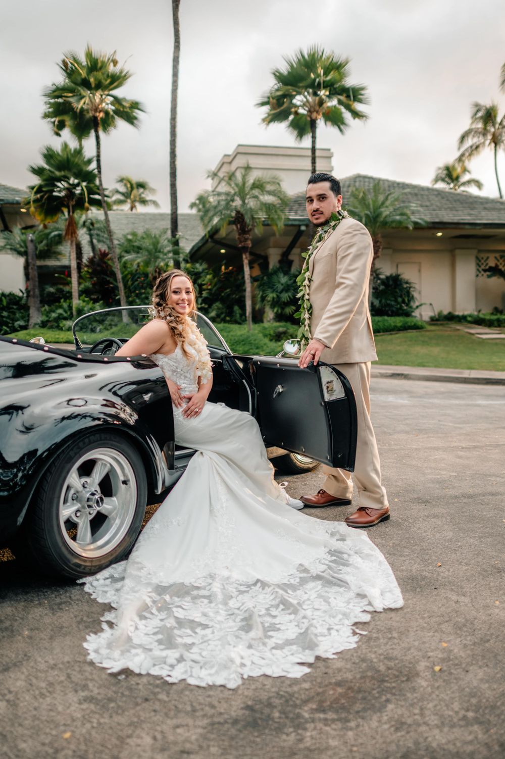 Bride and groom create romantic portraits with classic car in tropical setting.
