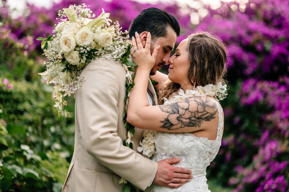 Romantic wedding couple embraces among vibrant purple bougainvillea flowers.