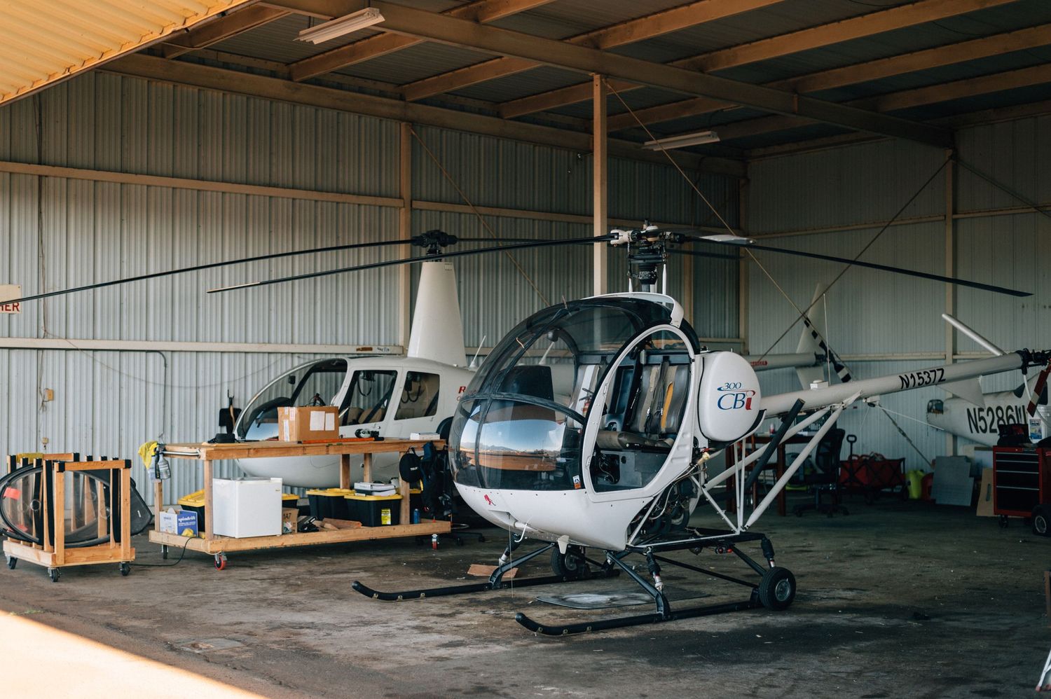 Multiple helicopters and small aircraft stored inside a large hangar.