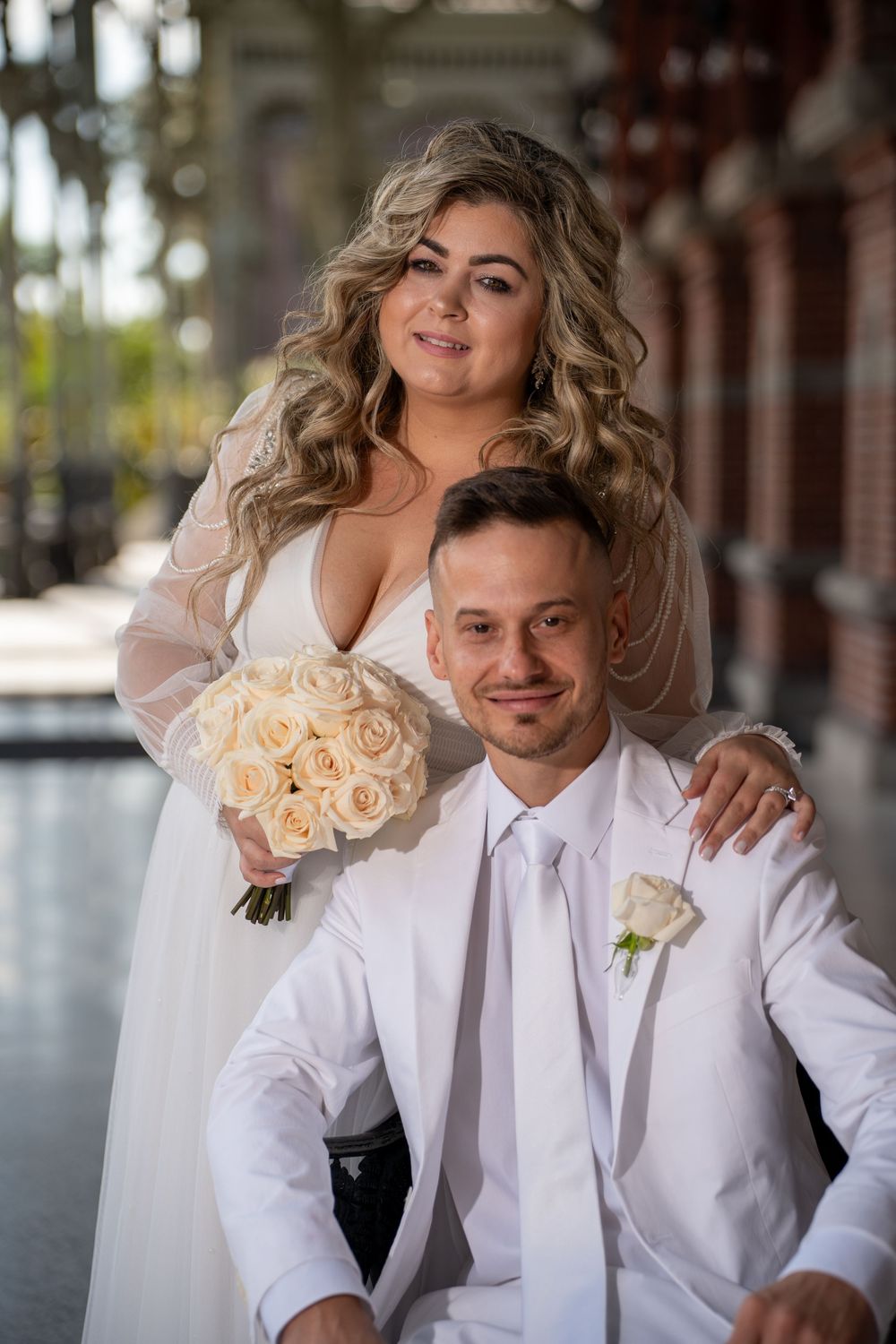 A couple poses together on their wedding day, with the bride holding a bouquet of cream roses.