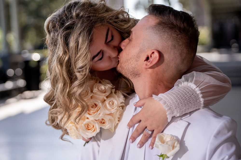 A romantic couple sharing a tender kiss outdoors in natural sunlight while wearing white clothing.