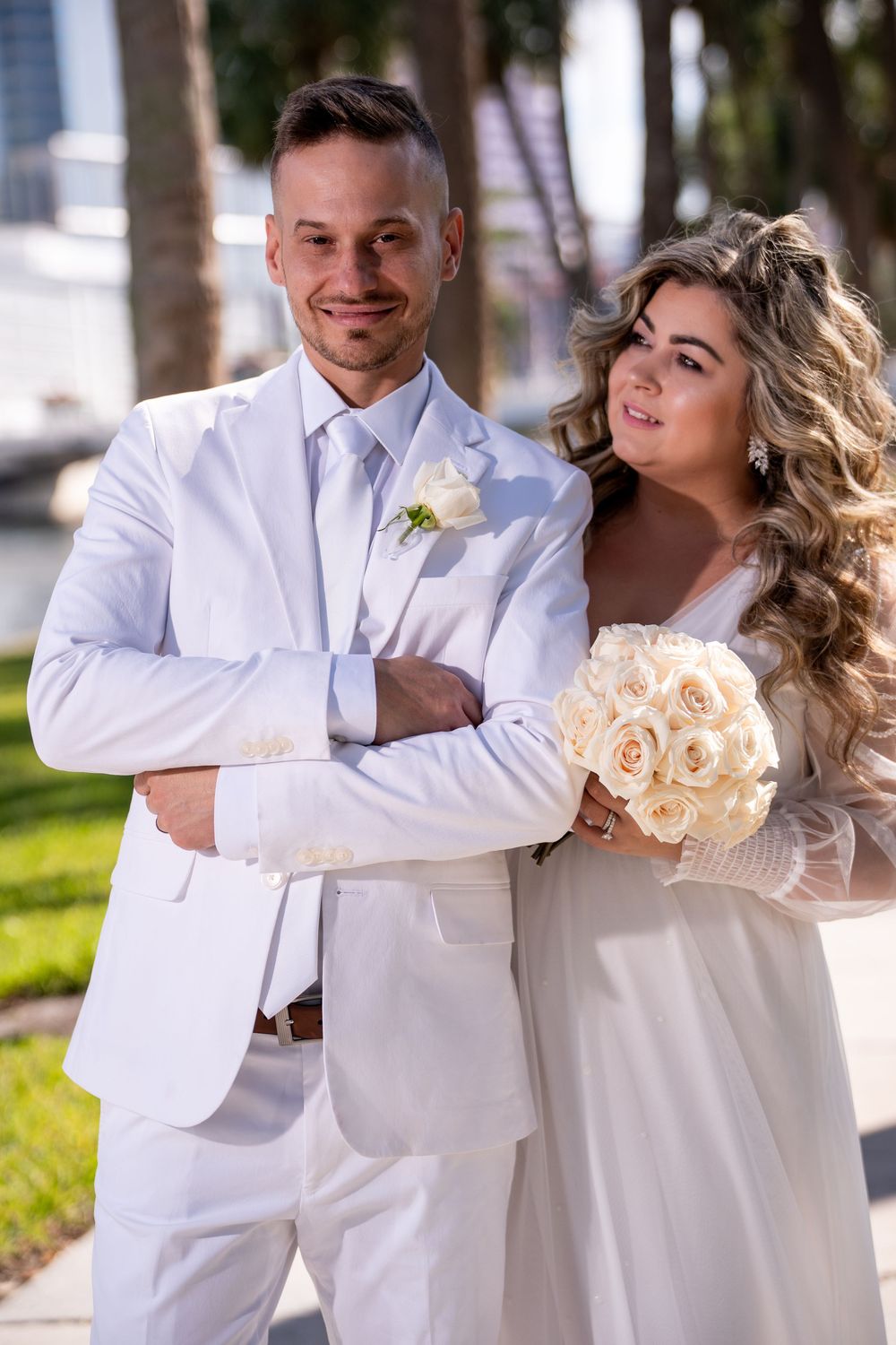 A romantic wedding couple in white attire embraces outdoors in a series of candid poses with peach-colored bouquet.