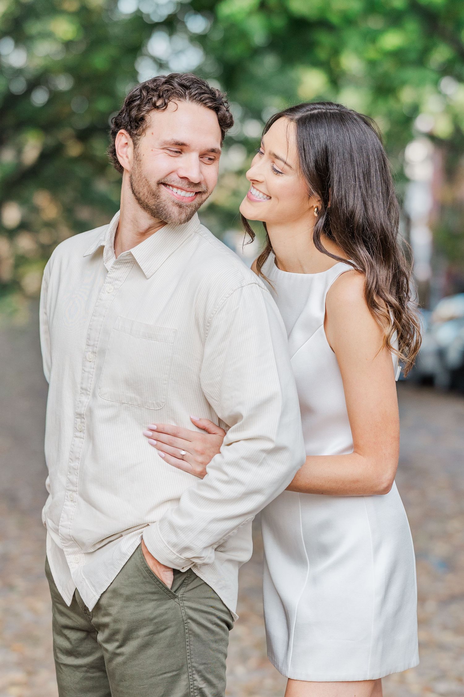 A couple in white outfits share joyful moments and laughter during a romantic outdoor photoshoot.