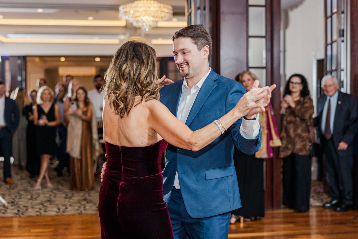 A couple dances together in an elegant ballroom with guests watching in the background.