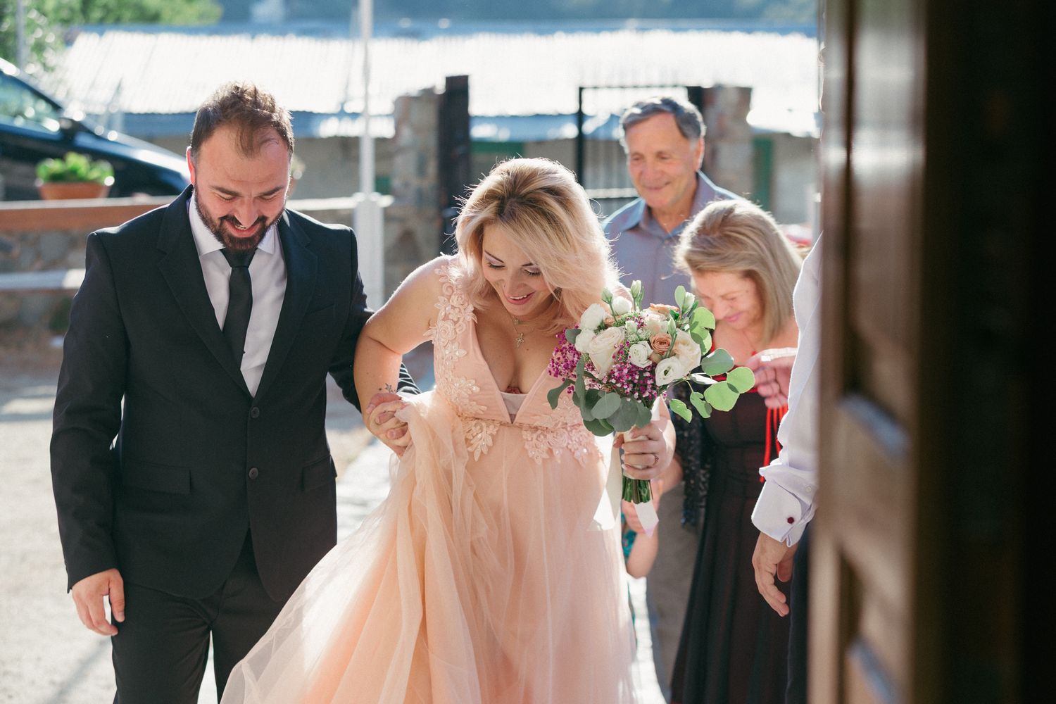 A group in formal attire walks together, with someone wearing a flowing peach-colored gown in the center.