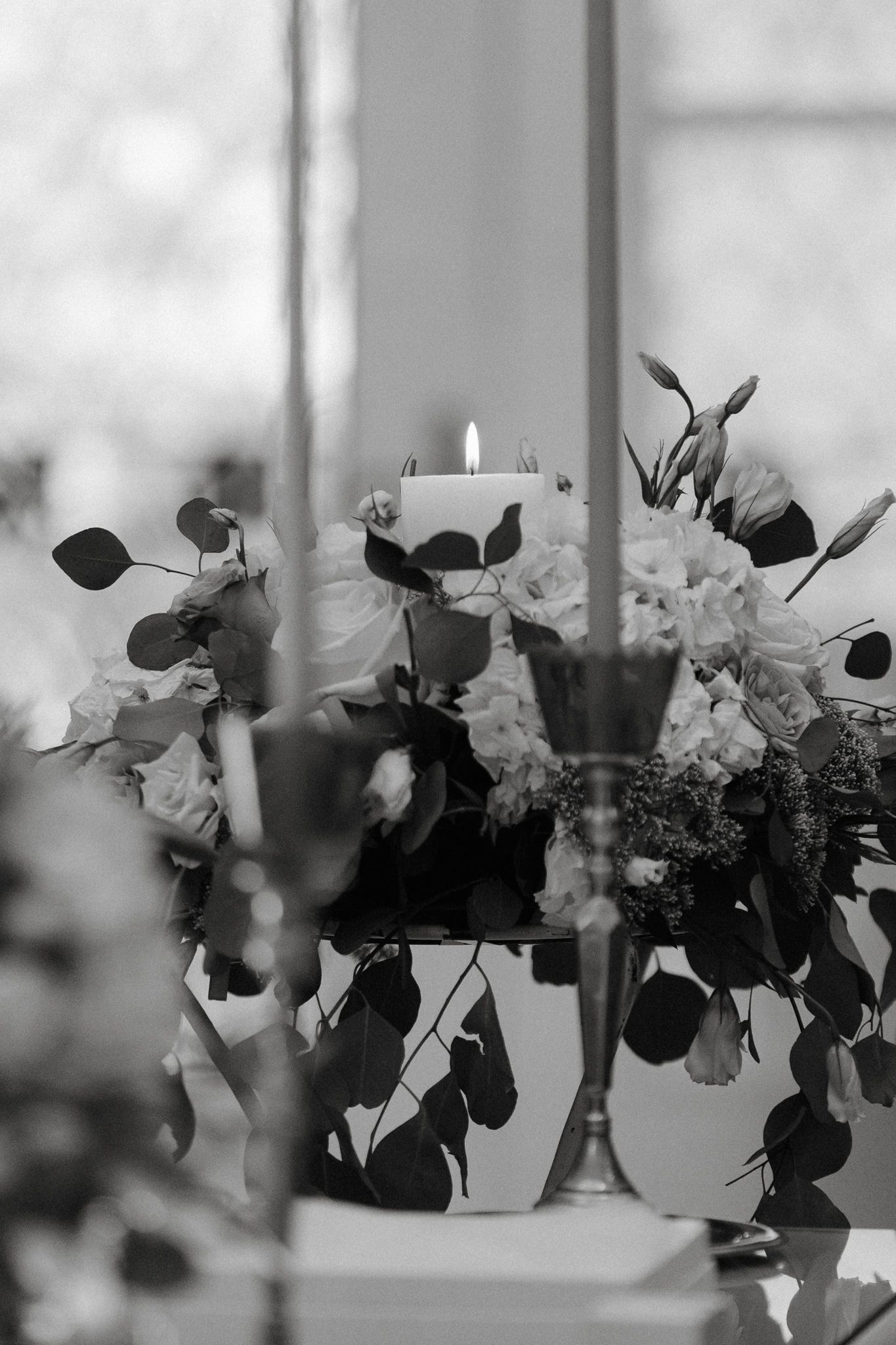 Black and white photograph of elegant floral centerpieces arranged in a row on a windowsill.