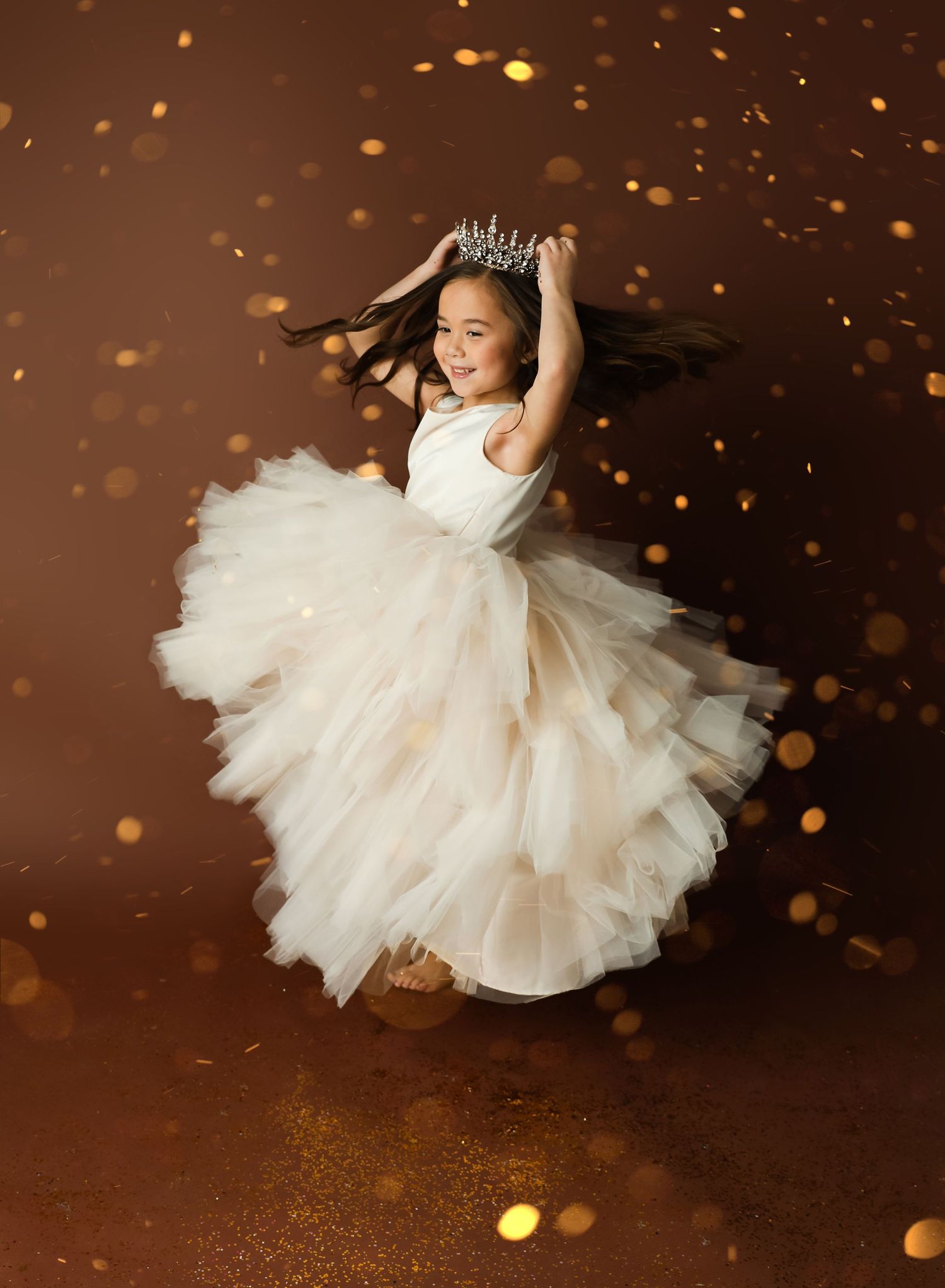 A small dancer in a flowing white tulle dress twirls gracefully under magical golden bokeh lights.