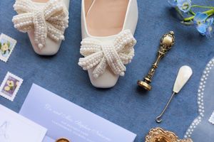 Flat lay of wedding accessories including bows, shoes, pearls, and decorative items on a blue fabric background.