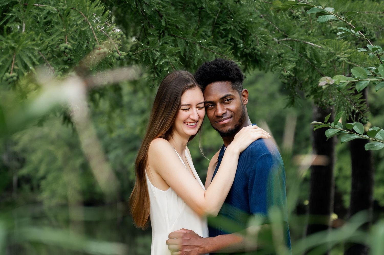 Couple sharing affectionate moments surrounded by green foliage in a park.