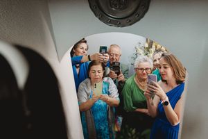 A group of people using smartphones to capture the bride’s first look during an indoor gathering