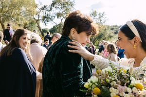 Wedding guests gather outdoors under trees at a sunny garden celebration with yellow floral accents.