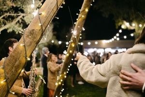 String lights illuminate a rustic outdoor wedding reception with guests mingling under trees at night.