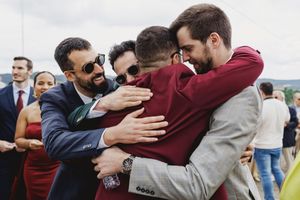 A group of friends embrace in a warm group hug outdoors on a wedding day.