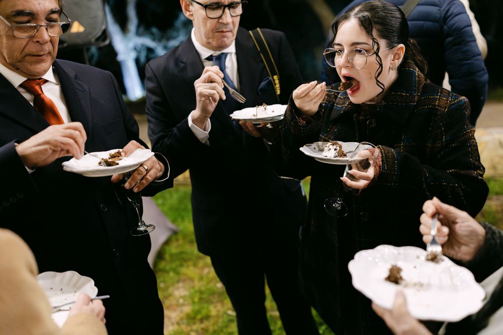People eating and socializing outdoors while holding plates of food at a wedding