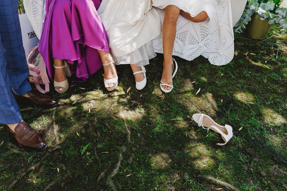 A row of wedding guests' feet and shoes lined up on grass during an outdoor celebration.