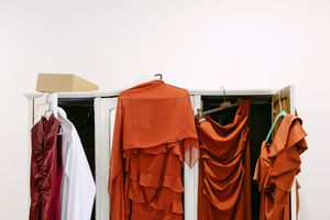 Colorful dresses hanging on a clothing rack featuring warm tones of burgundy, orange and rust against a white wall during a wedding