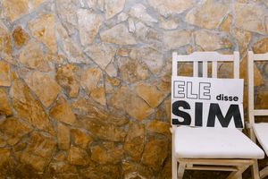White wooden chair against textured stone wall with text 'He said yes' displayed on paper, during a wedding in lisbon