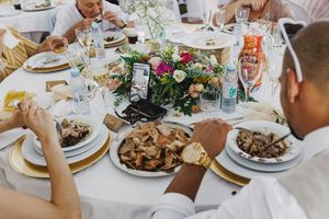 People enjoying a festive meal at a wedding traditional portuguese set table with floral centerpieces and plates of food.