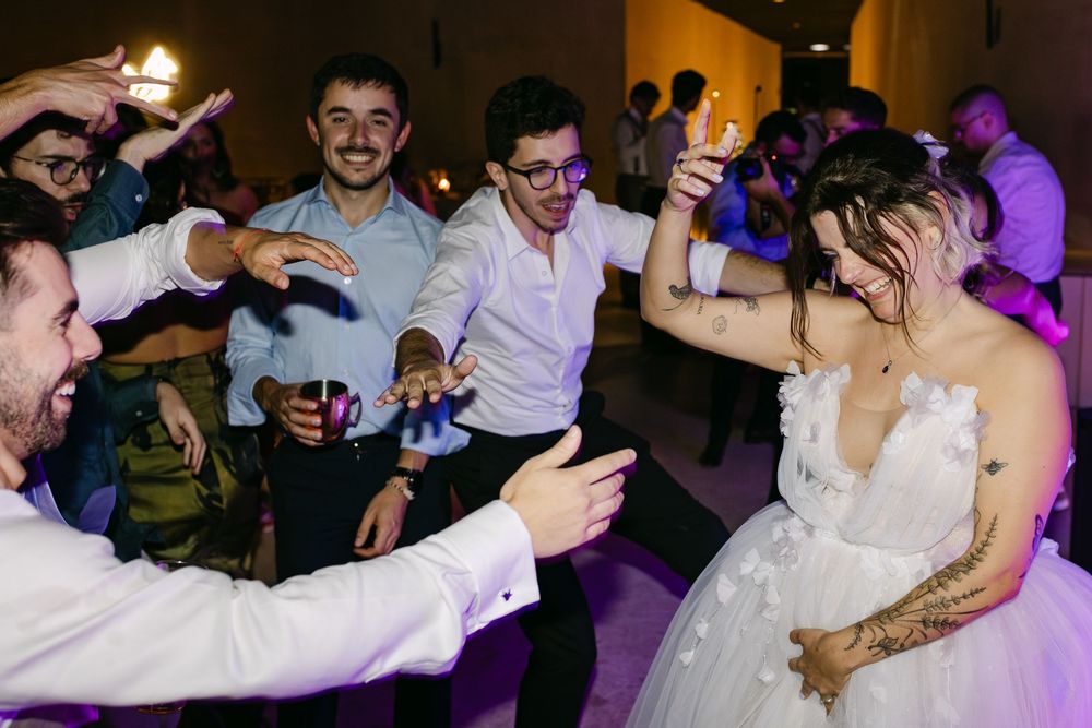 Guests dance and celebrate on a lively dance floor at a wedding reception with purple lighting in the background.