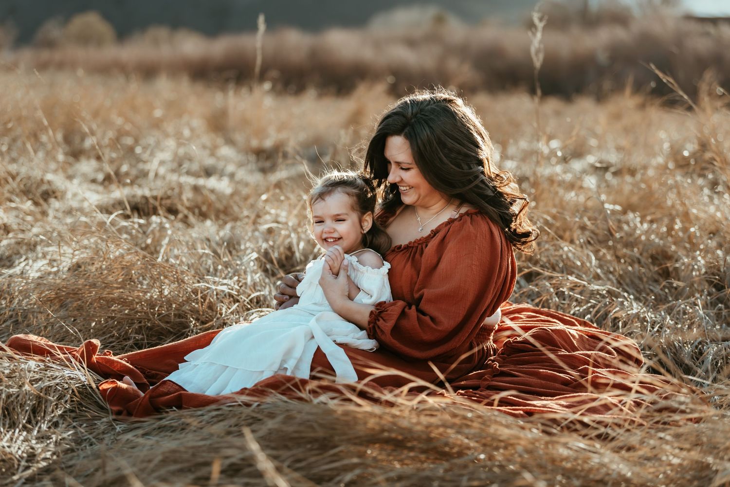 Autumn outdoor portrait with figure in rust-colored dress holding baby in white.