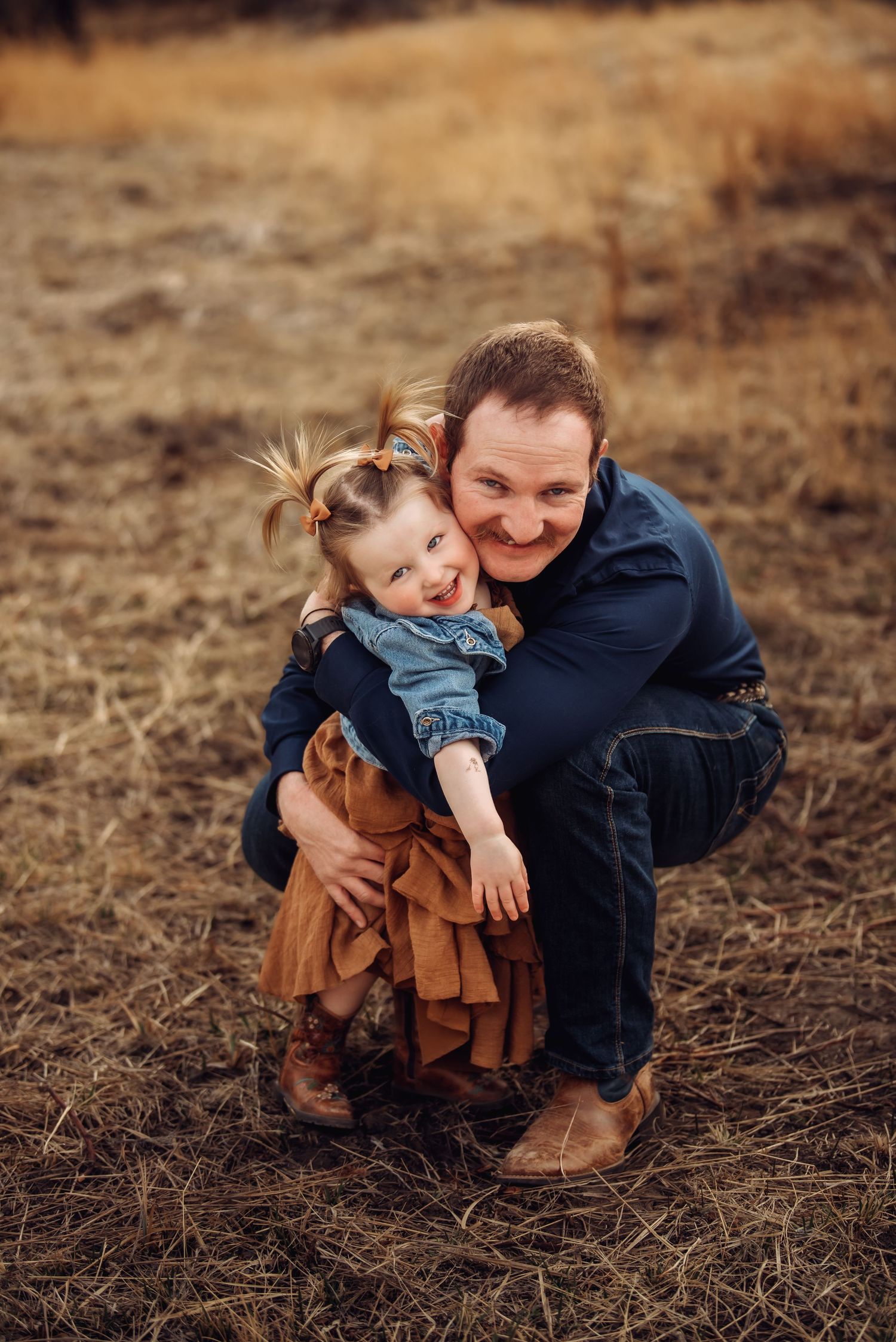 A parent and child share a tender moment together while crouching in a brown field during autumn.