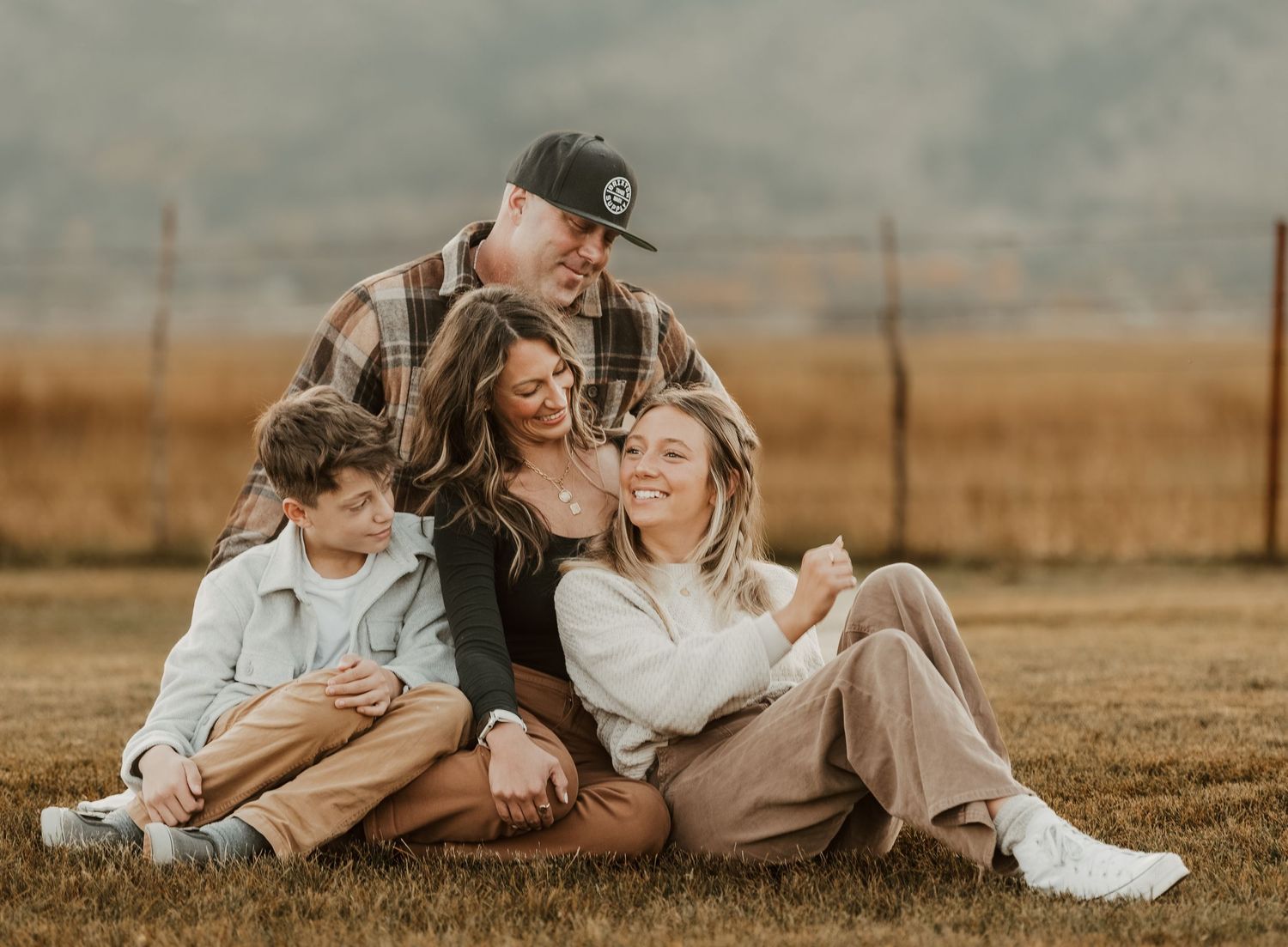 A loving family moment captured in warm autumn tones as they sit together on grassy field at sunset.
