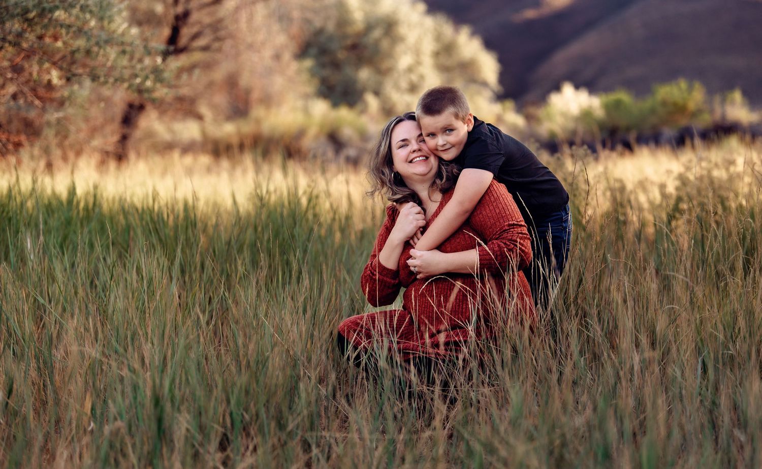 A couple embraces in a romantic outdoor photoshoot among tall grass at golden hour.