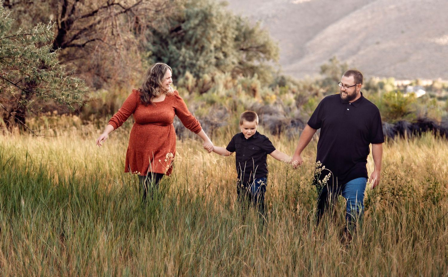 A family joyfully runs through a golden field at sunset with mountains in the background.
