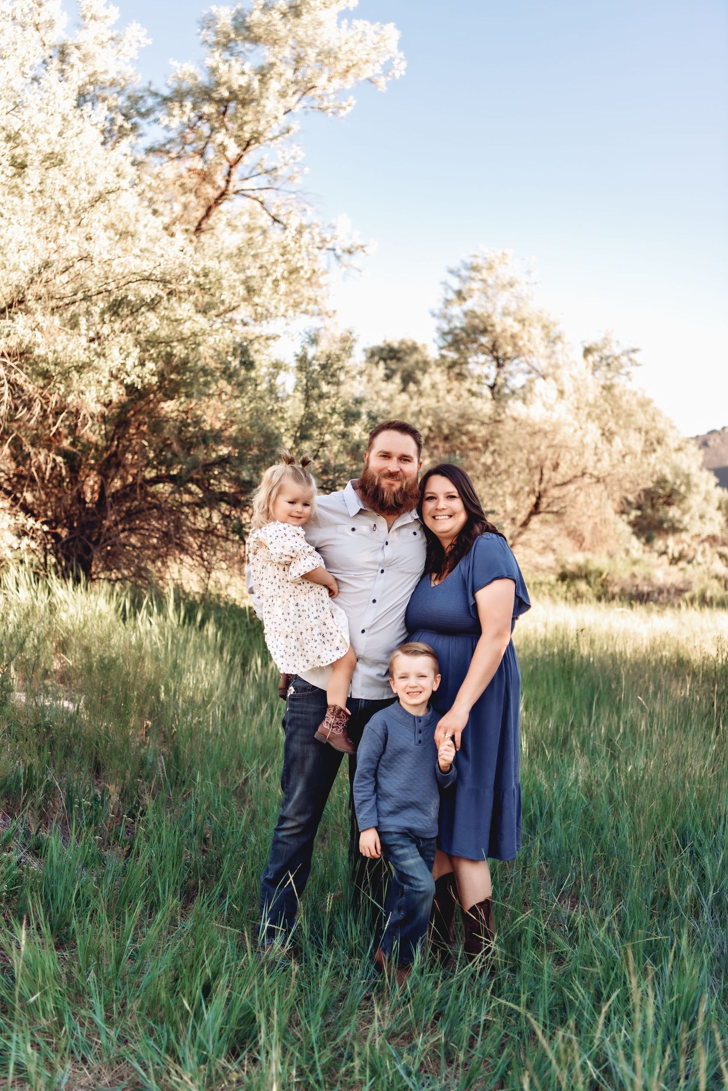 A family poses together in a grassy field during golden hour with trees in the background.