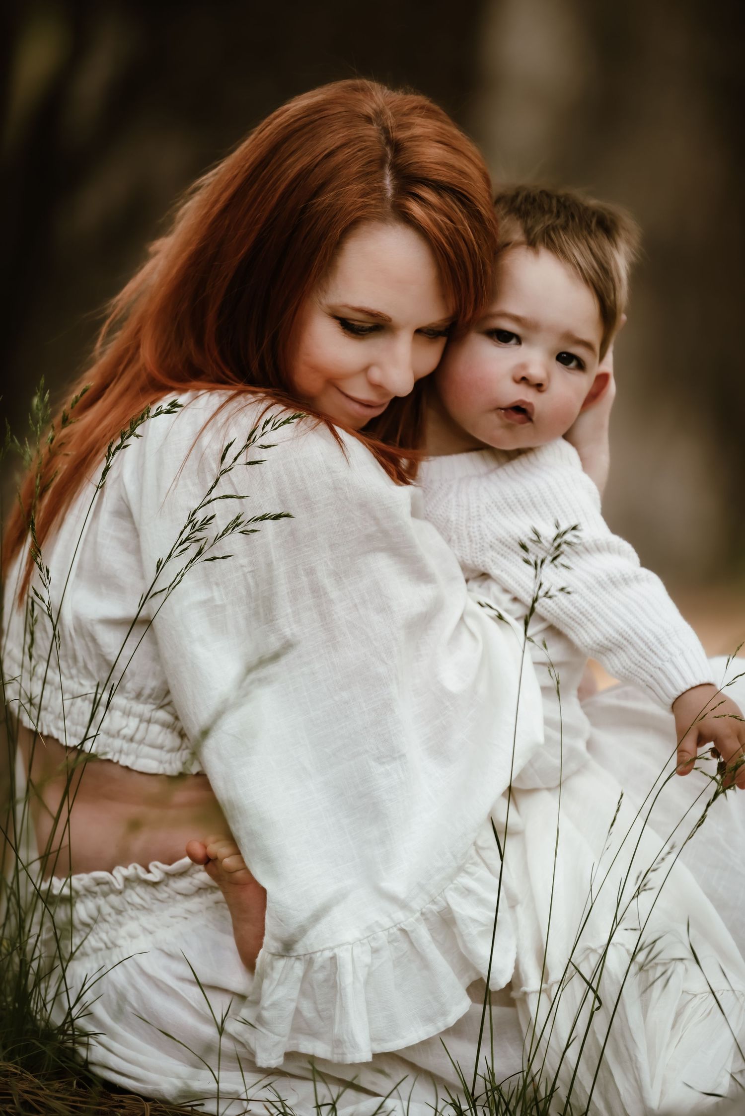 A tender moment between mother and child in white dresses amidst tall grasses.
