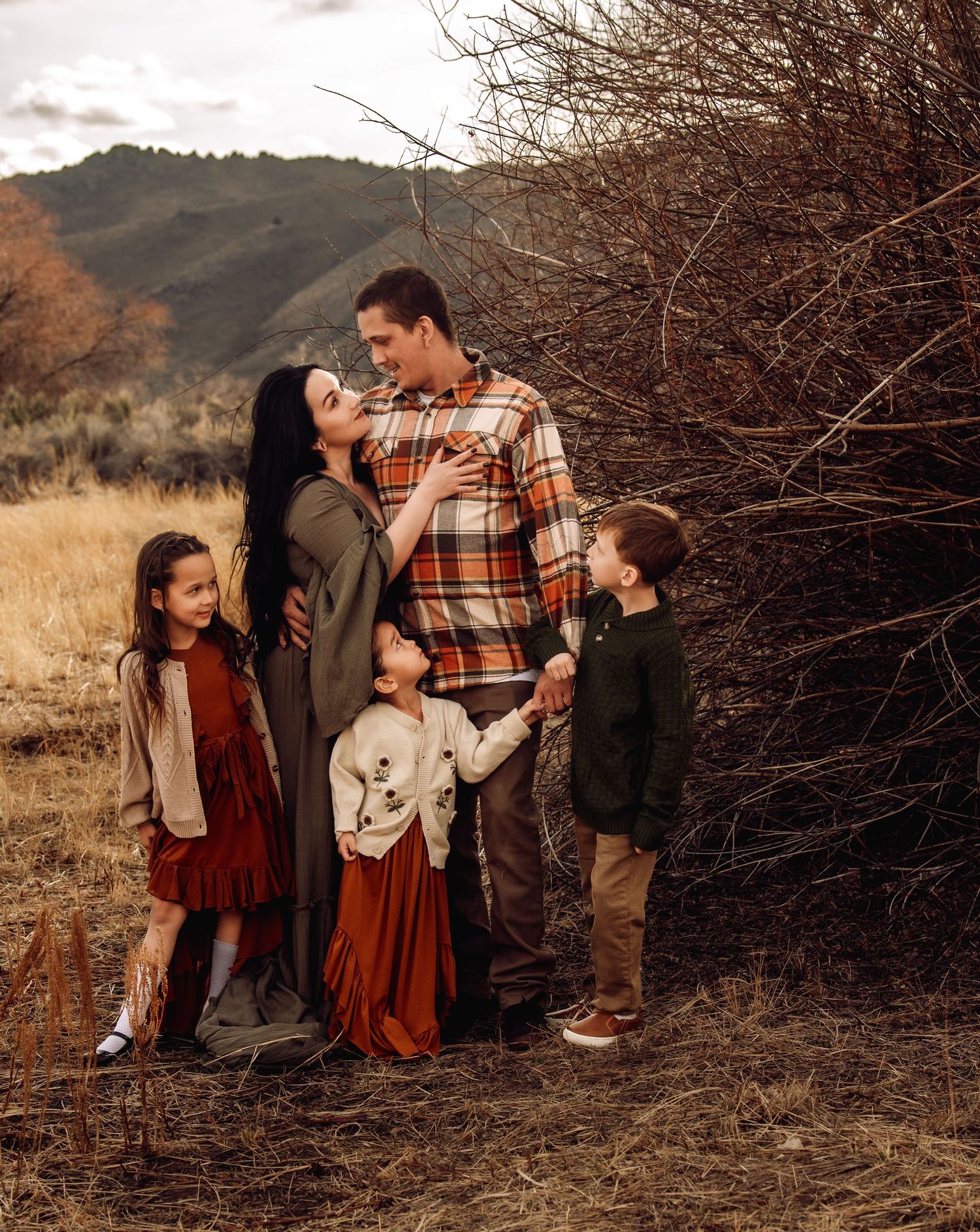 A family shares playful moments together during an outdoor photo session in a rustic autumn setting.