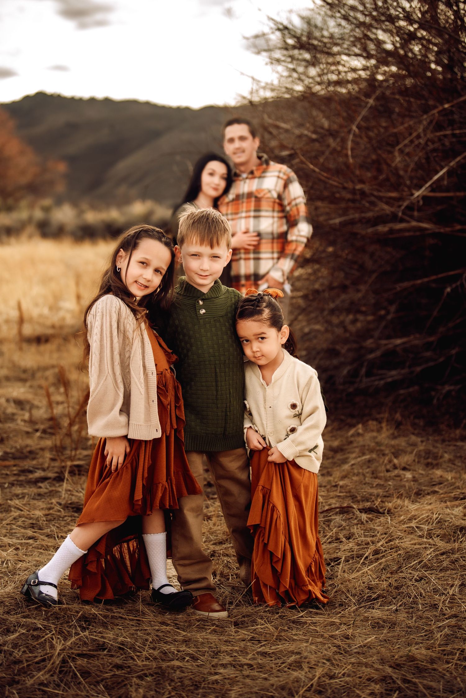 Three children in vintage-inspired autumn outfits play together in a rustic outdoor setting at golden hour.