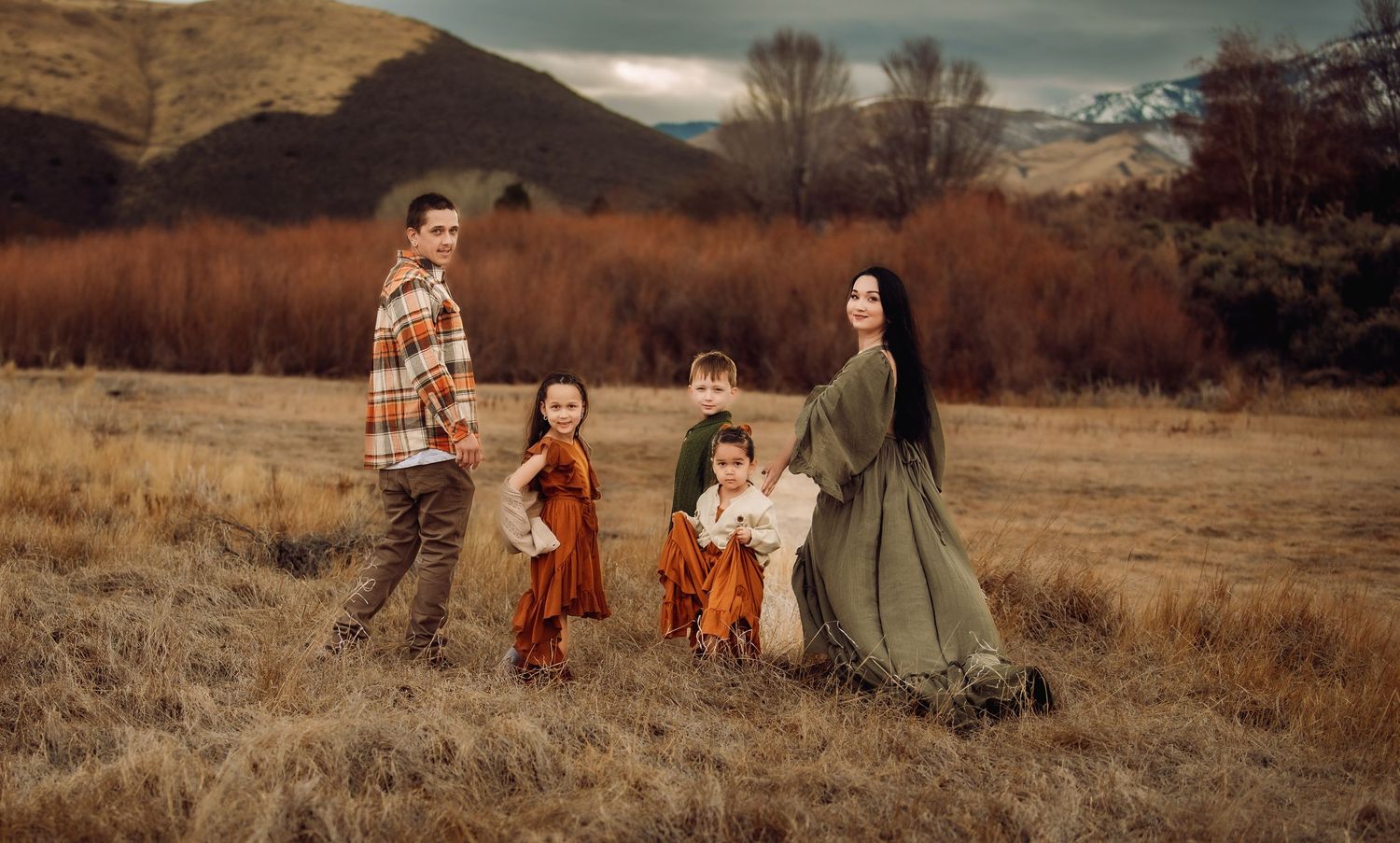 A group in vintage-inspired outfits poses in a golden autumn field at sunset creating a nostalgic scene.
